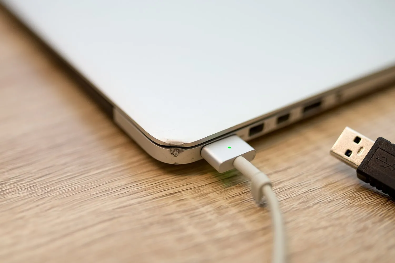 A laptop charging from a USB cable on a wooden table